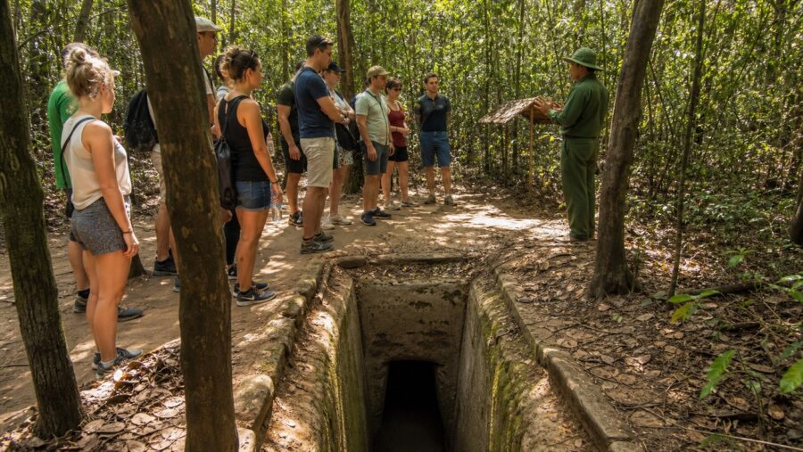 Guided visitor group near a Cu Chi Tunnels entrance in a tropical forest